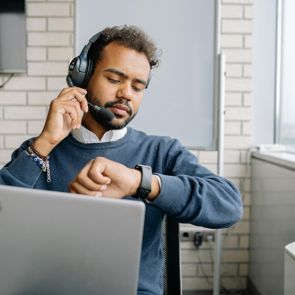 Man with headset checking time on smartwatch at his desk.