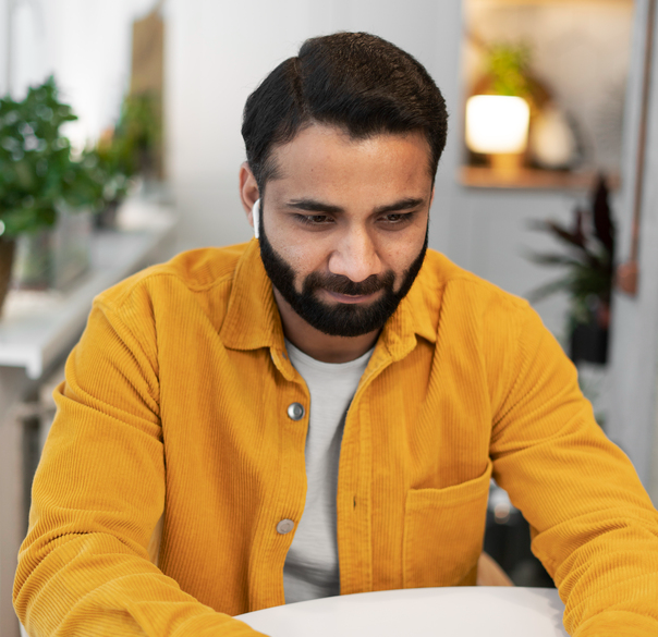 Young man in a stylish yellow shirt concentrated on his work at a table in a bright indoor environment.